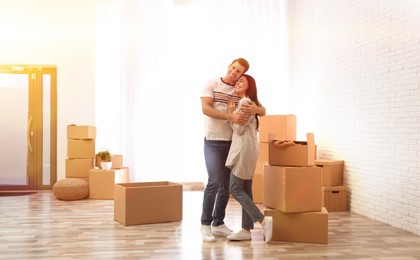 Image of Happy couple in sunlit room with cardboard boxes on moving day