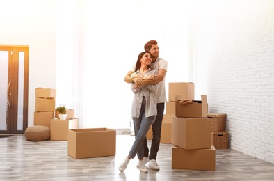 Image of Happy couple in sunlit room with cardboard boxes on moving day