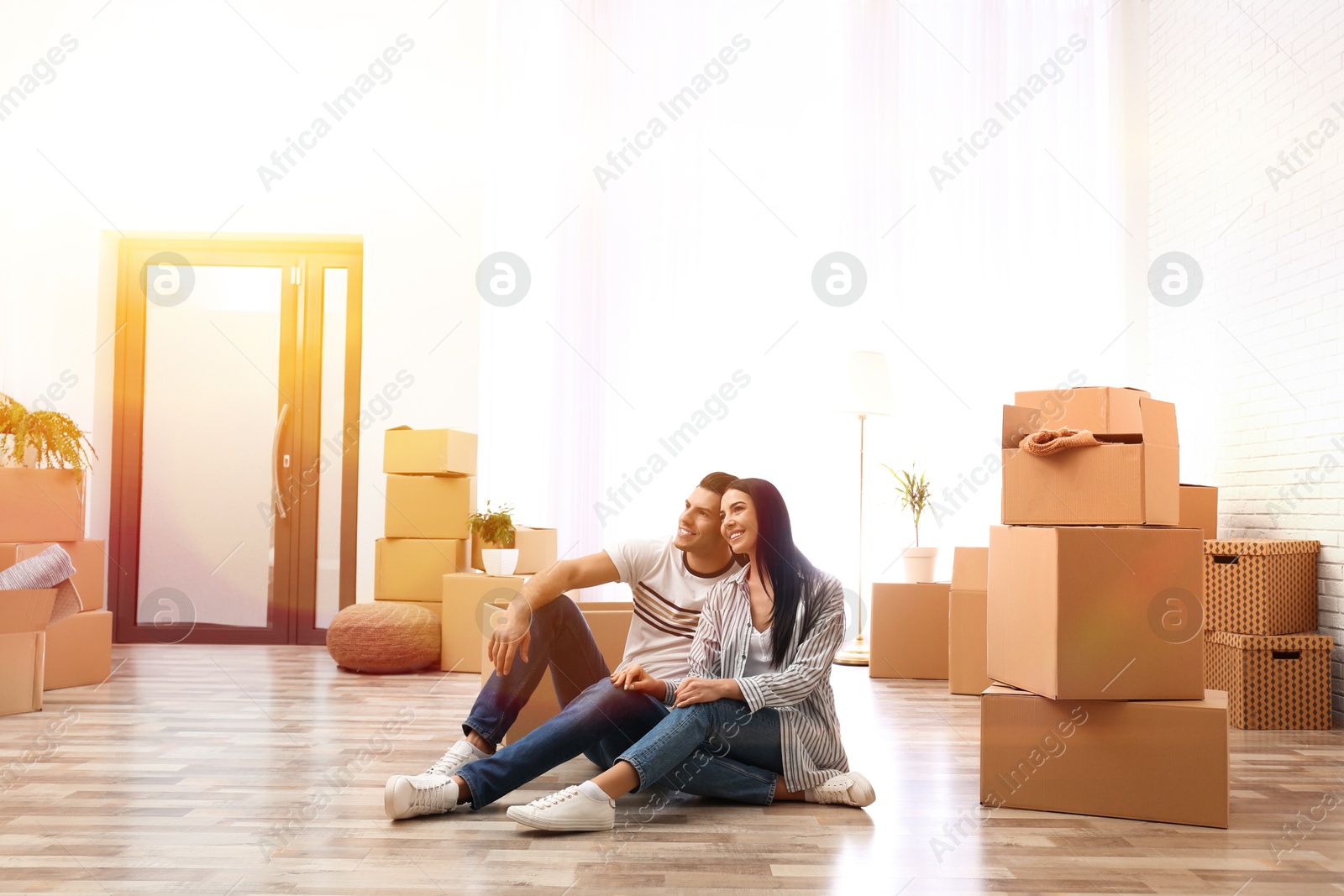 Image of Happy couple in sunlit room with cardboard boxes on moving day