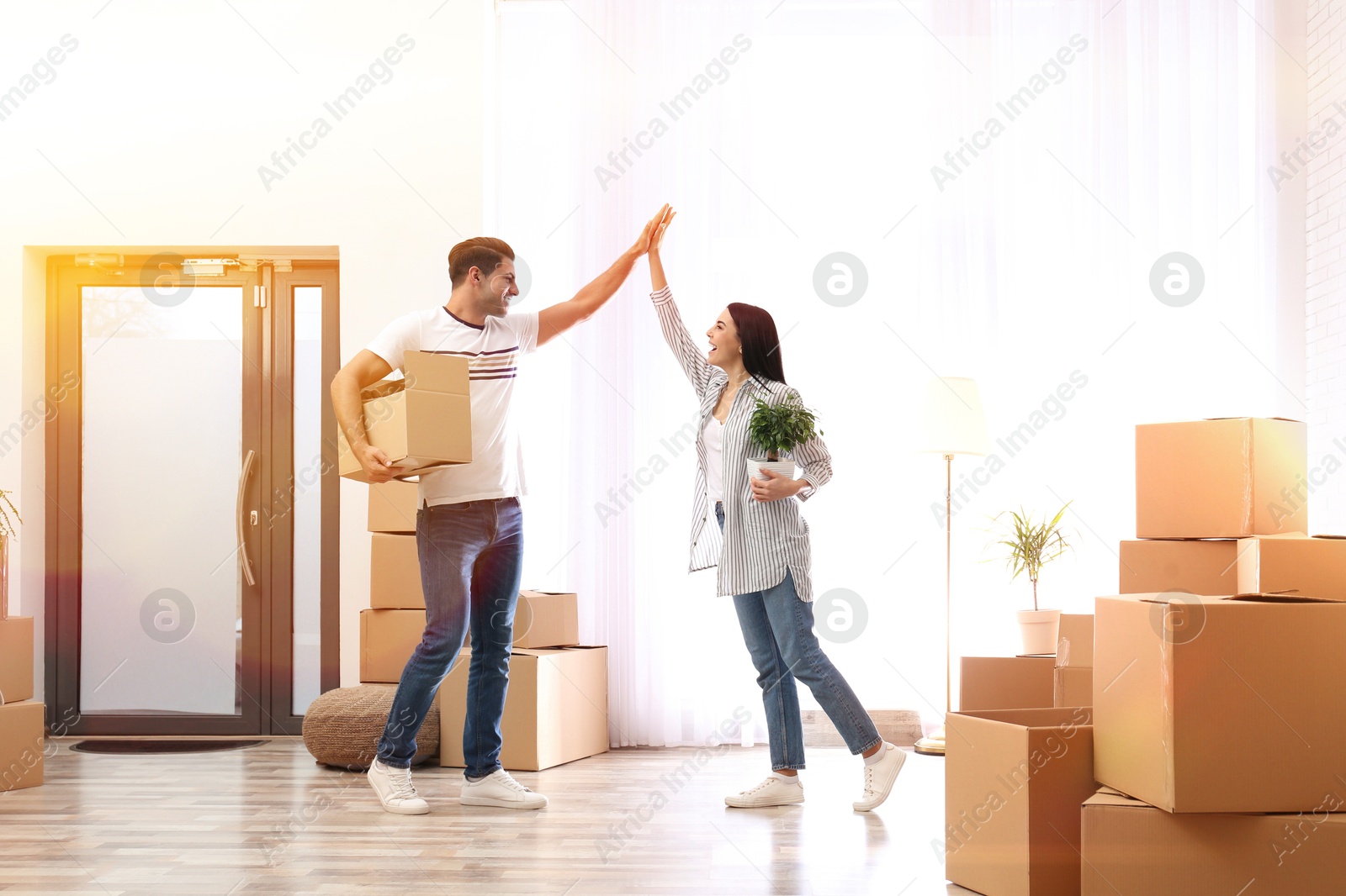 Image of Happy couple in sunlit room with cardboard boxes on moving day