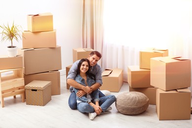 Image of Happy couple in sunlit room with cardboard boxes on moving day