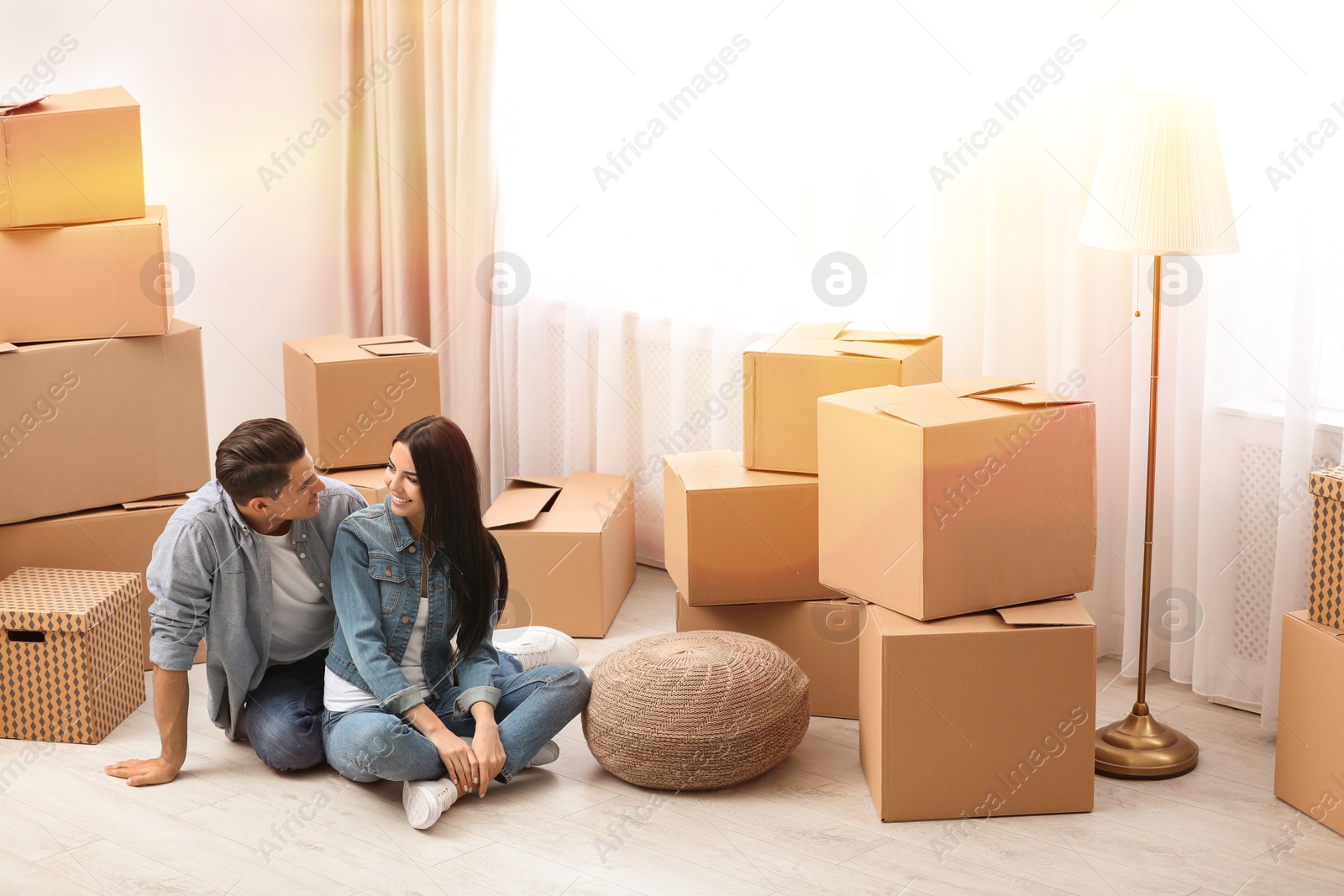 Image of Happy couple in sunlit room with cardboard boxes on moving day