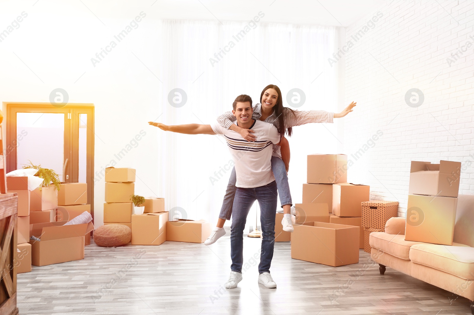 Image of Happy couple in sunlit room with cardboard boxes on moving day