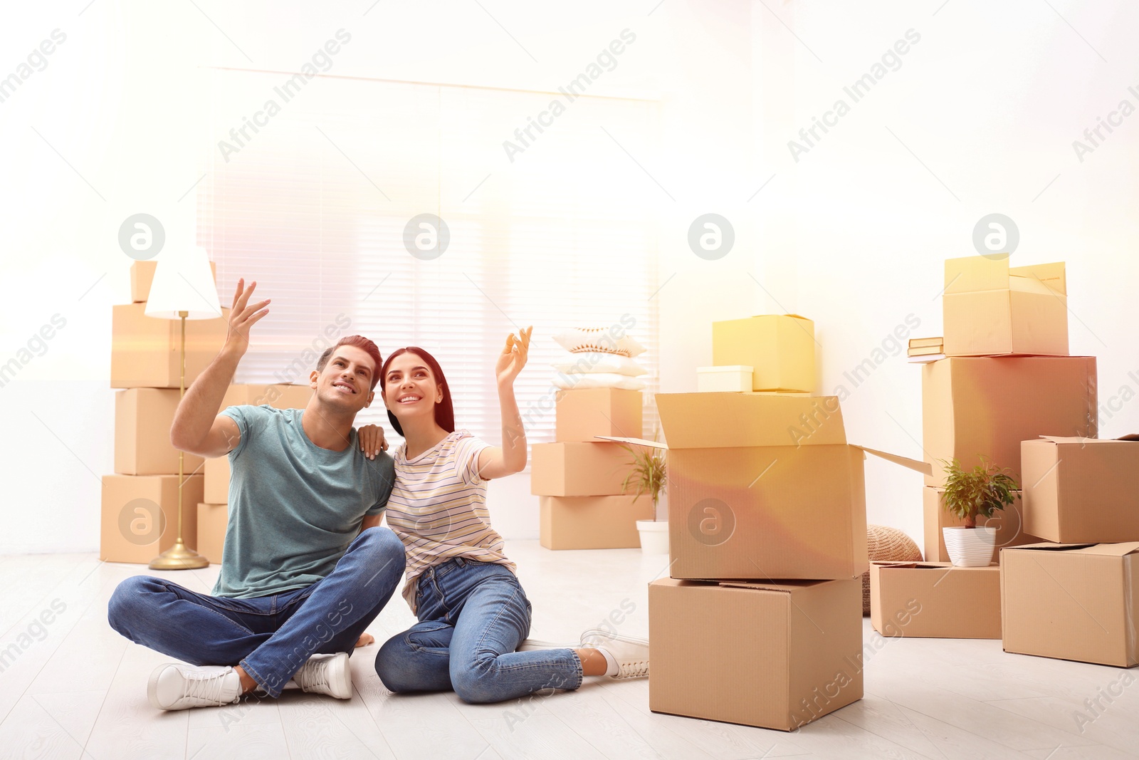 Image of Happy couple in sunlit room with cardboard boxes on moving day