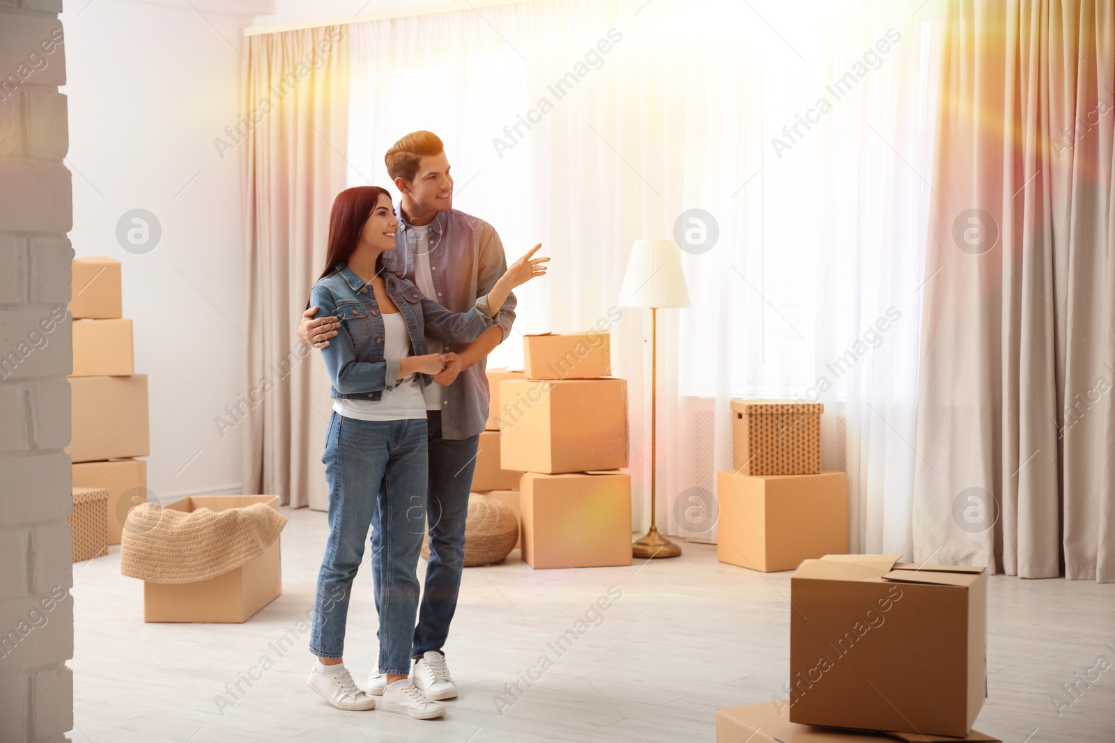 Image of Happy couple in sunlit room with cardboard boxes on moving day