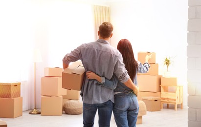 Image of Happy couple in sunlit room with cardboard boxes on moving day