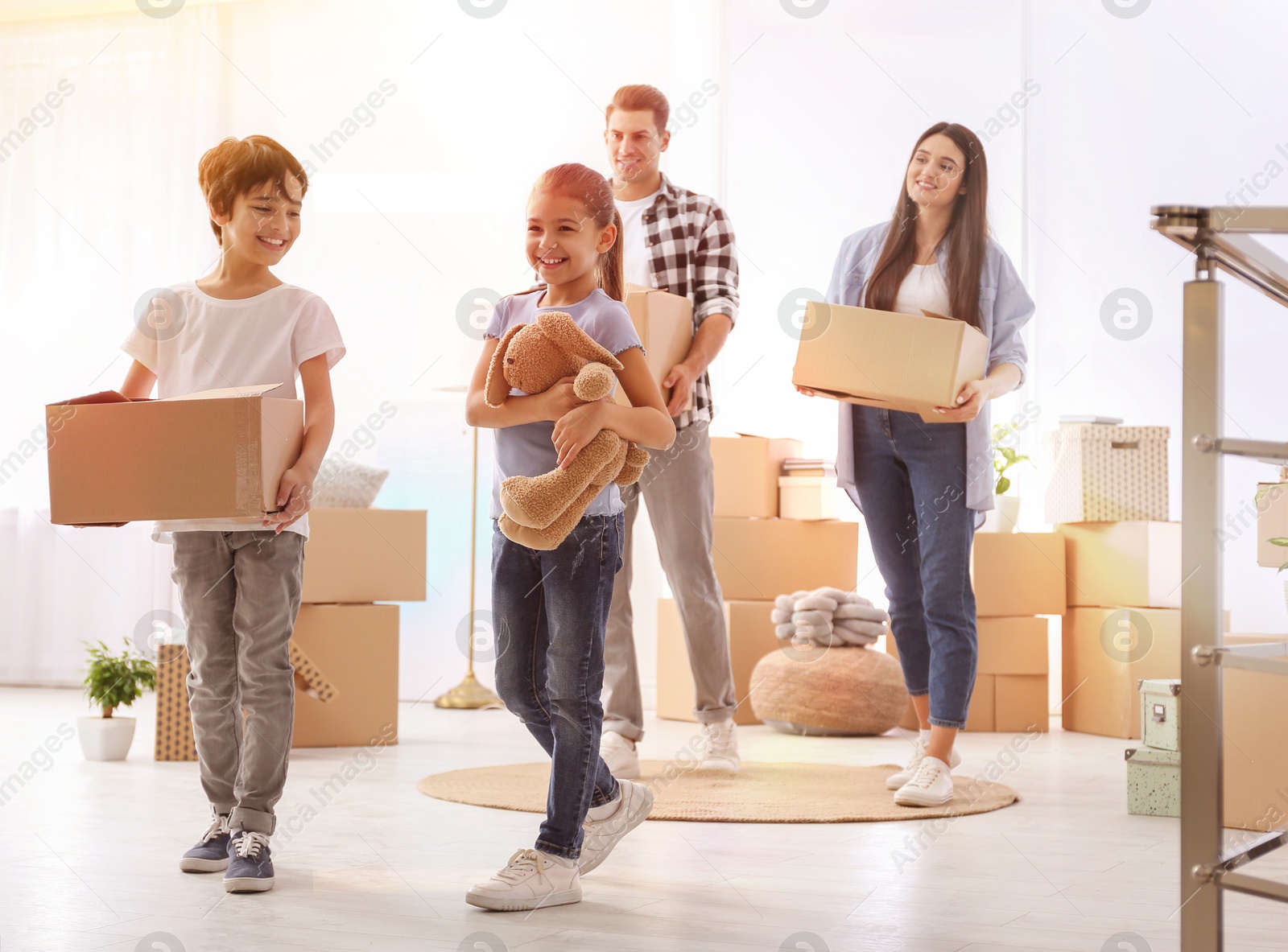 Image of Happy family in sunlit room with cardboard boxes on moving day