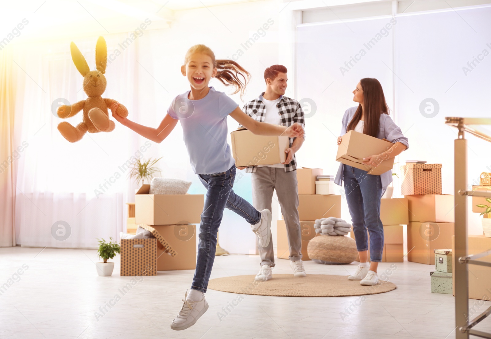 Image of Happy family in sunlit room with cardboard boxes on moving day