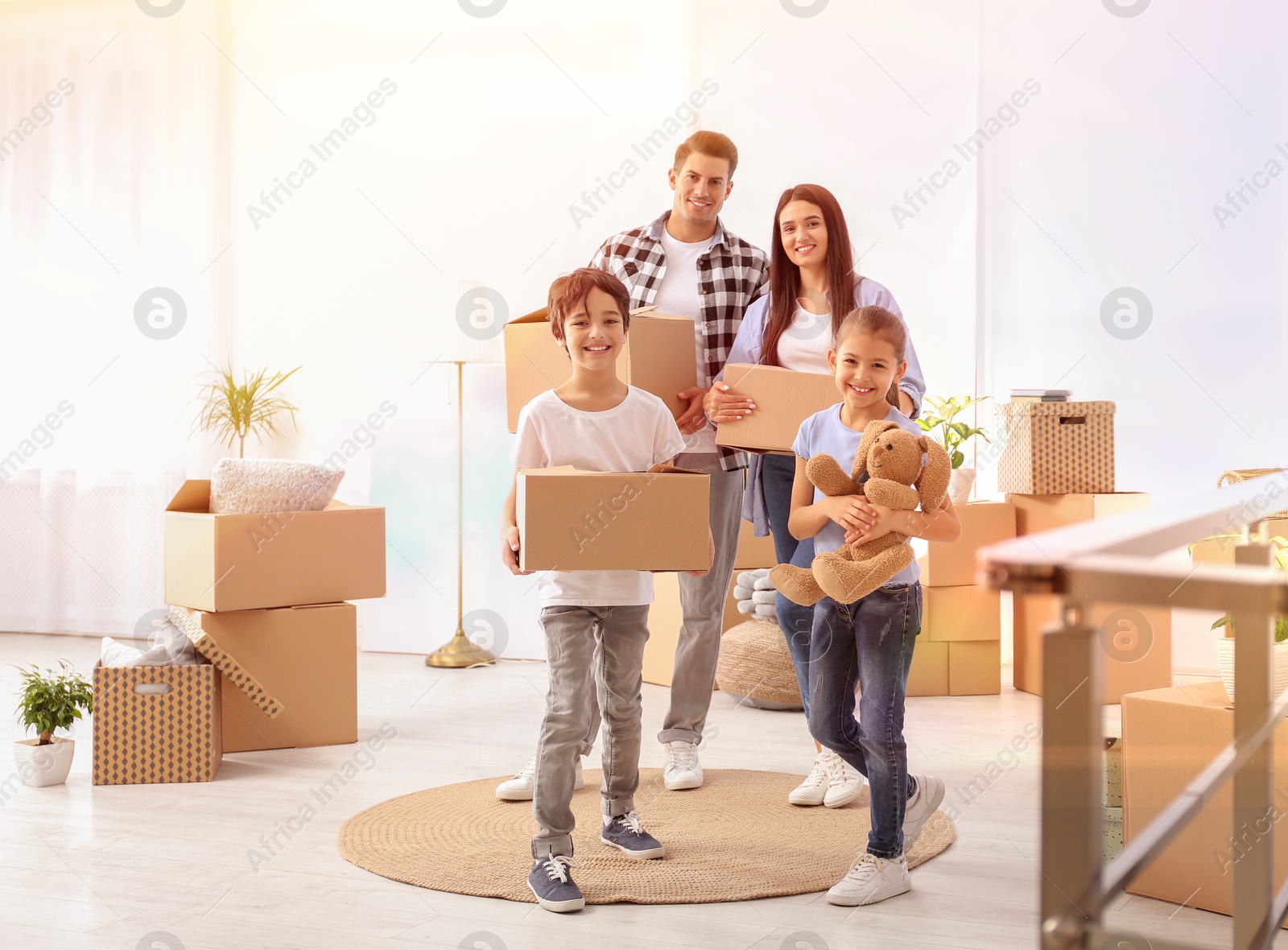 Image of Happy family in sunlit room with cardboard boxes on moving day