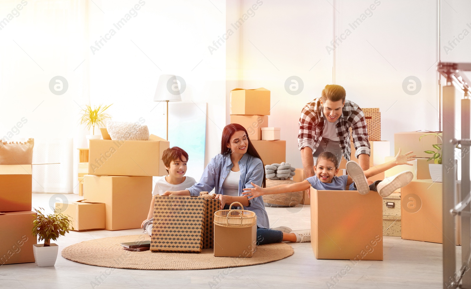 Image of Happy family in sunlit room with cardboard boxes on moving day