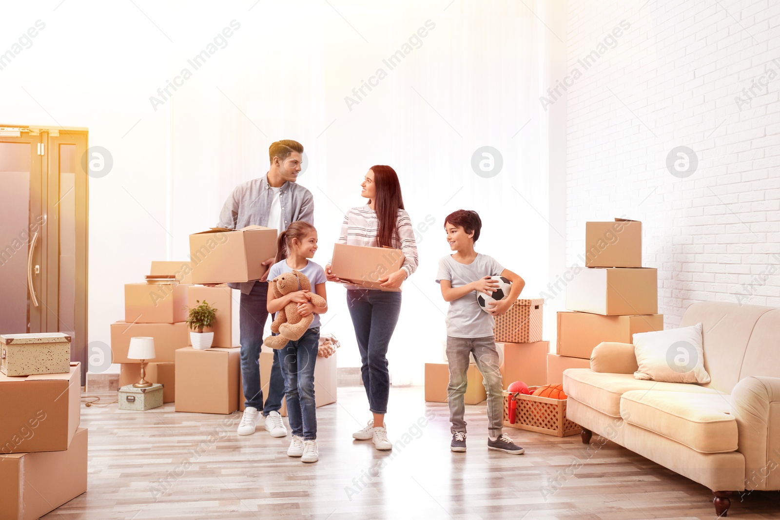 Image of Happy family in sunlit room with cardboard boxes on moving day