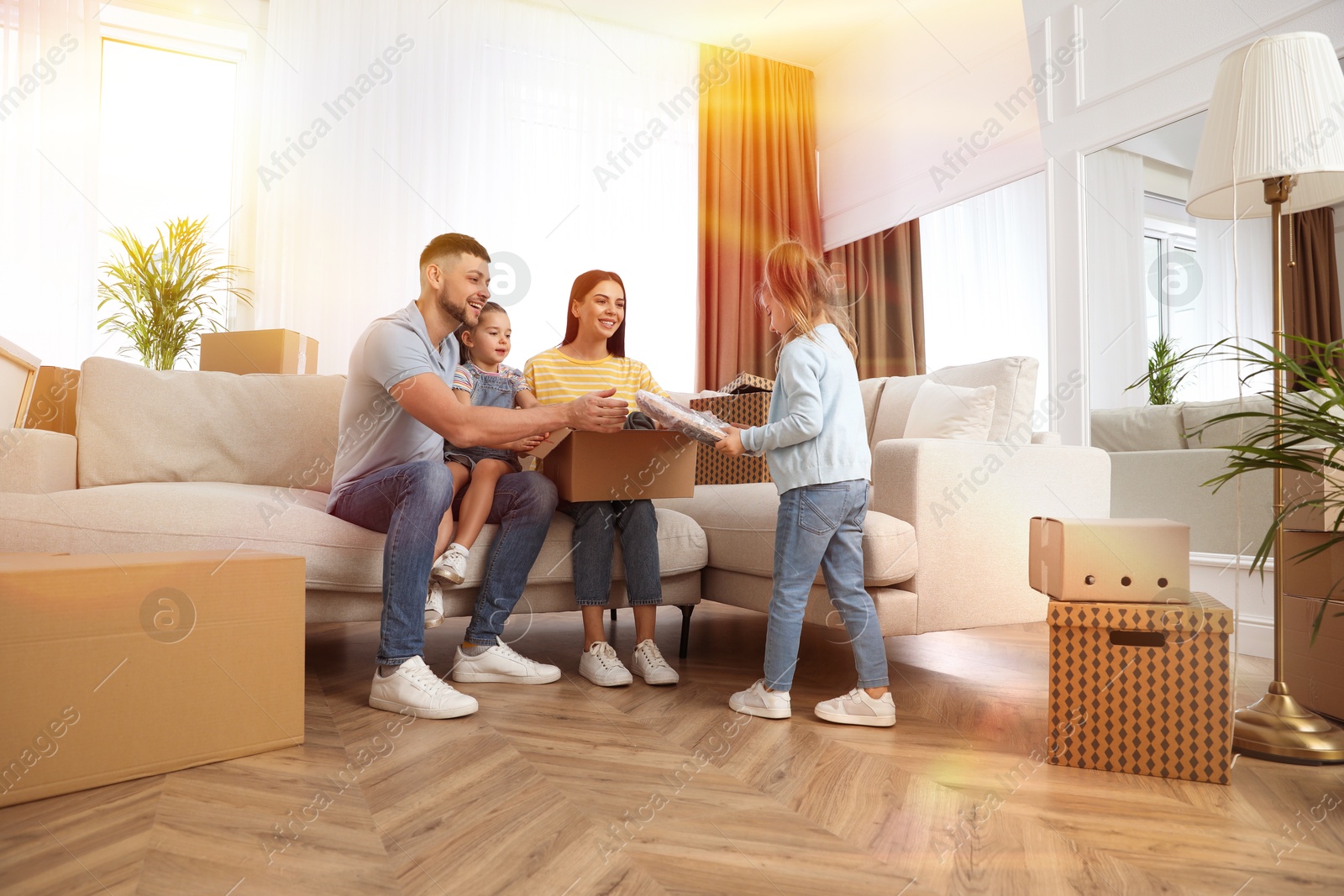 Image of Happy family in sunlit room with cardboard boxes on moving day