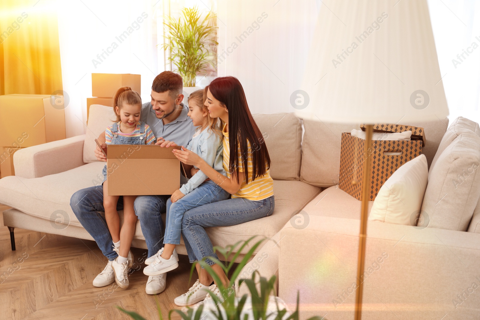 Image of Happy family in sunlit room with cardboard boxes on moving day