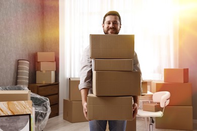 Image of Happy man holding cardboard boxes in sunlit room on moving day