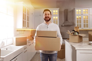 Image of Happy man holding cardboard boxes in sunlit kitchen on moving day