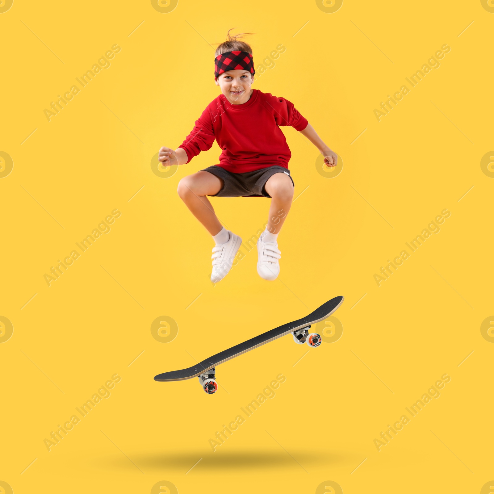 Image of Cute little boy with skateboard in air on yellow background. Performing trick