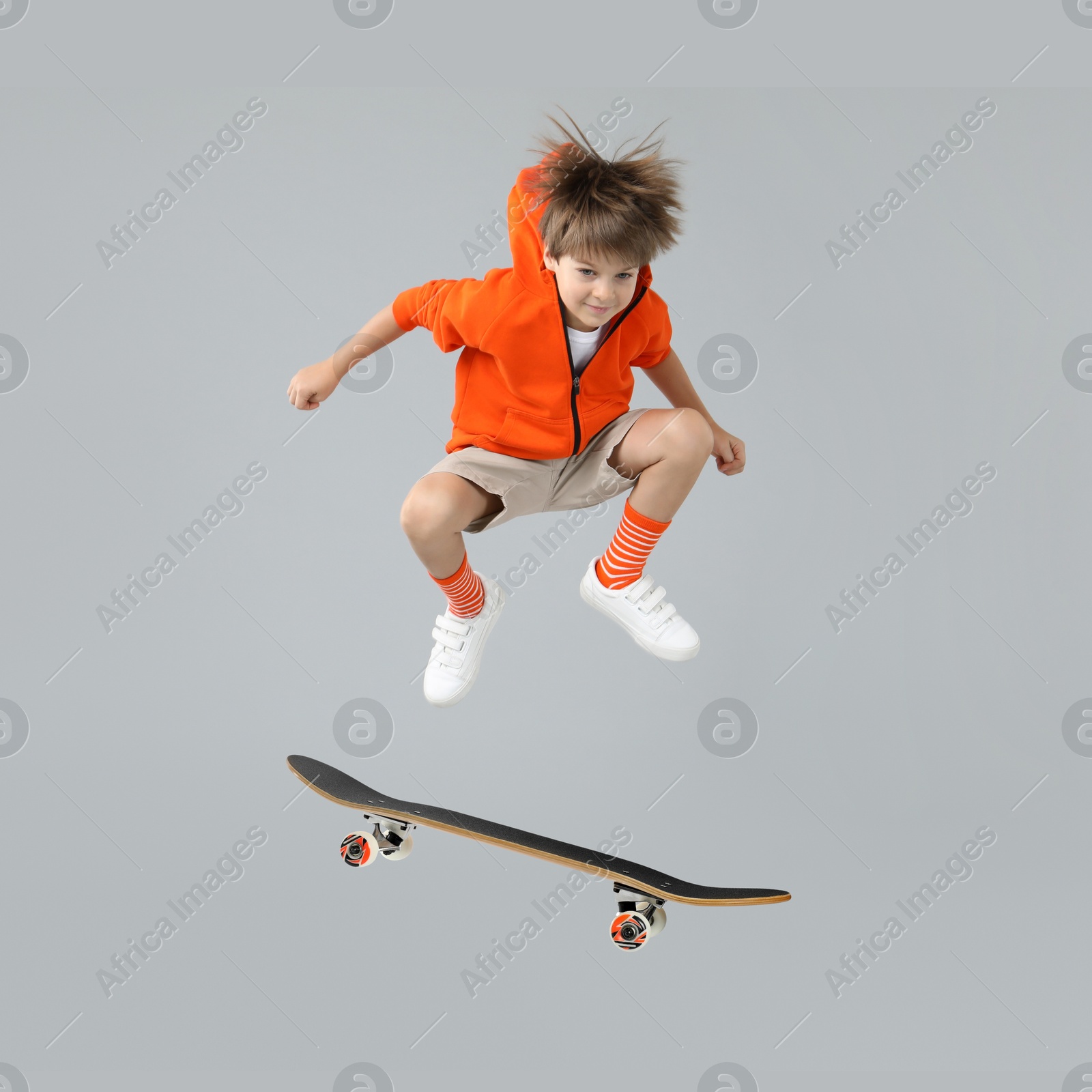 Image of Cute little boy with skateboard in air on grey background. Performing trick