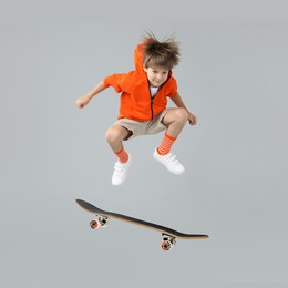 Image of Cute little boy with skateboard in air on grey background. Performing trick