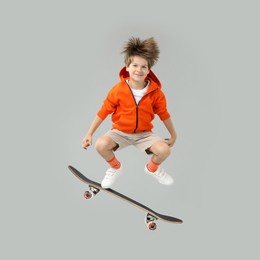 Image of Cute little boy with skateboard in air on grey background. Performing trick