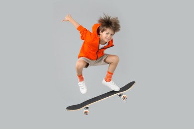 Cute little boy with skateboard in air on grey background. Performing trick