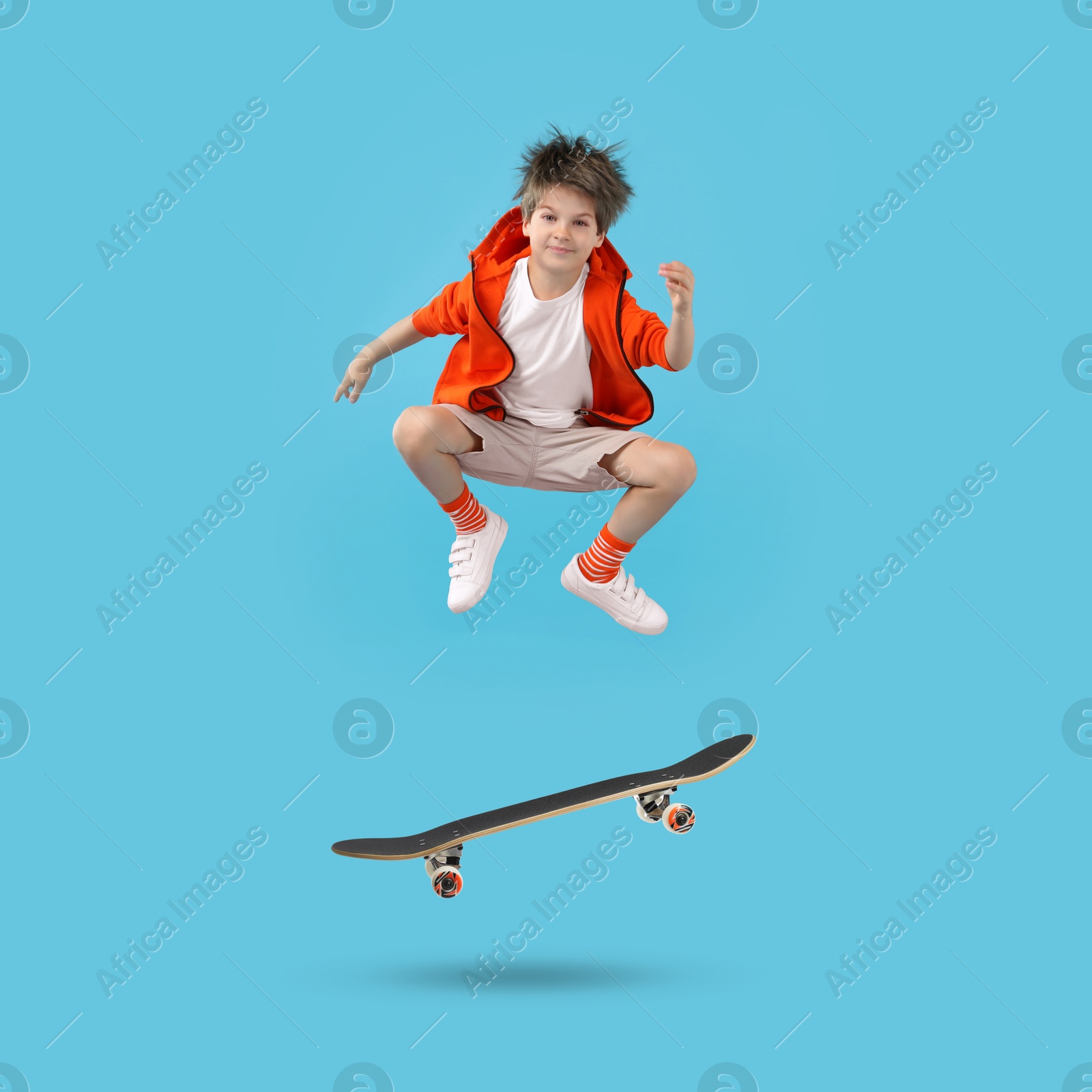 Image of Cute little boy with skateboard in air on light blue background. Performing trick