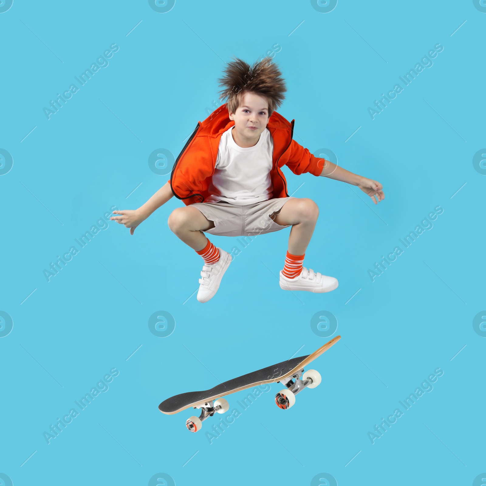 Image of Cute little boy with skateboard in air on light blue background. Performing trick