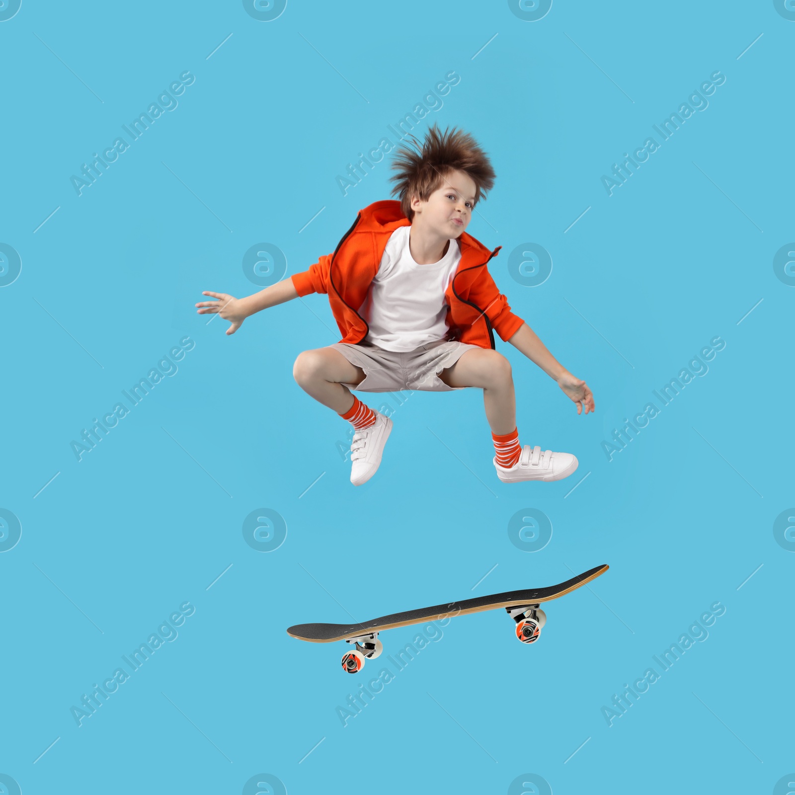 Image of Cute little boy with skateboard in air on light blue background. Performing trick