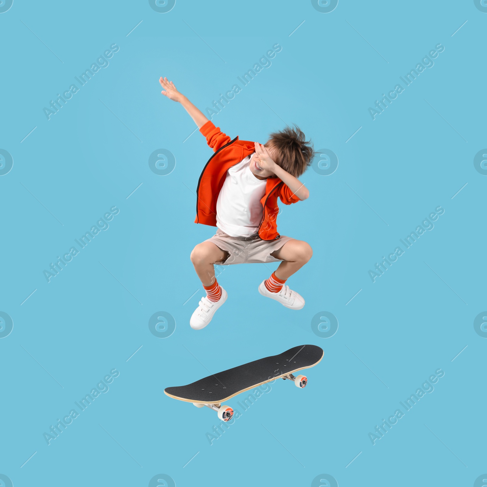 Image of Cute little boy with skateboard in air on light blue background. Performing trick