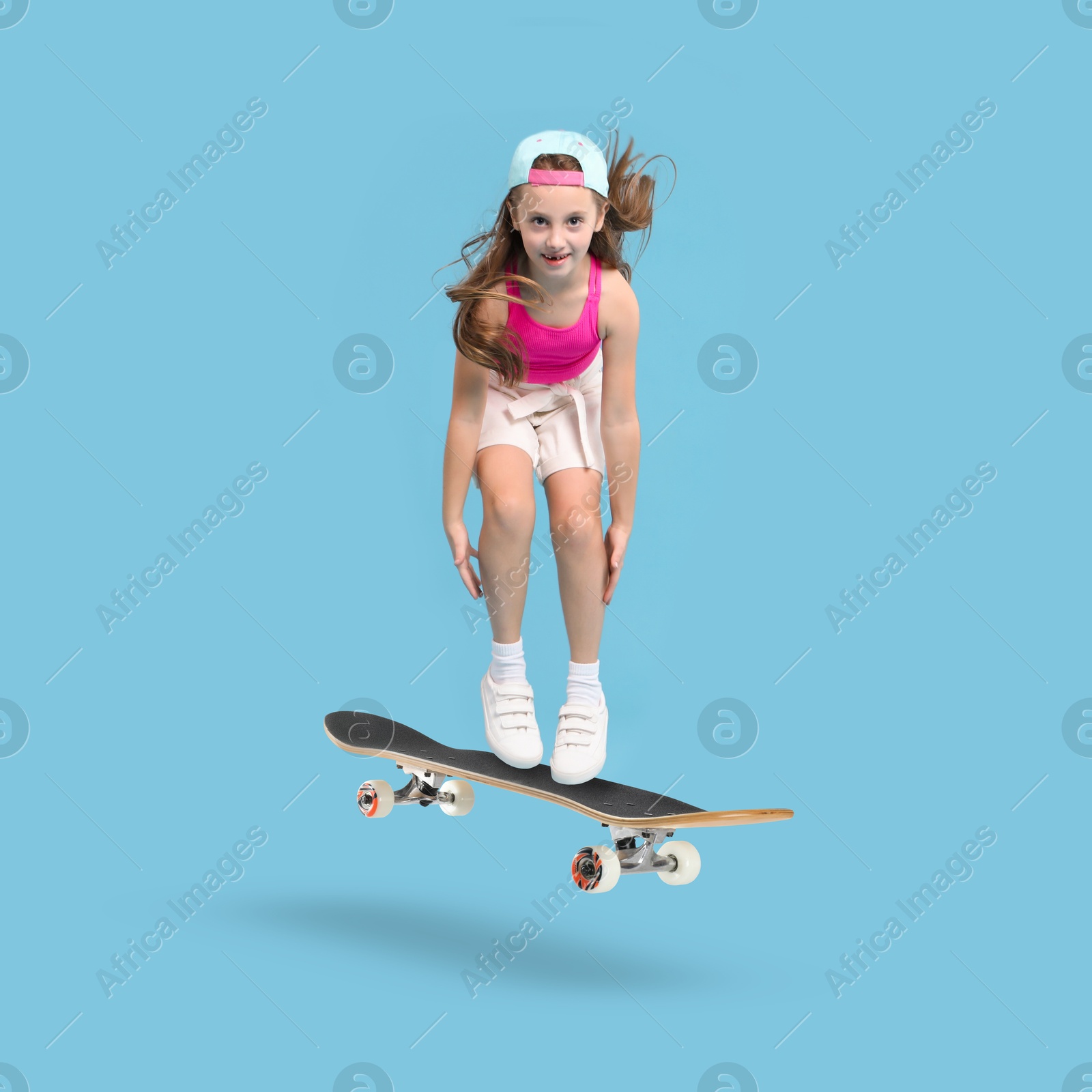 Image of Cute little girl with skateboard in air on light blue background. Performing trick