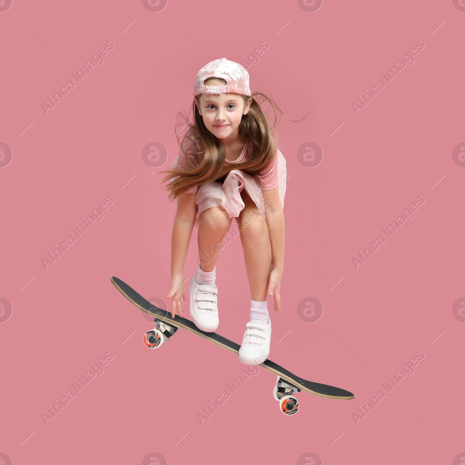 Image of Cute little girl with skateboard in air on pink background. Performing trick