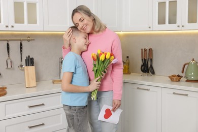 Photo of Happy Mother's Day. Son greeting his mom with flowers and card in kitchen