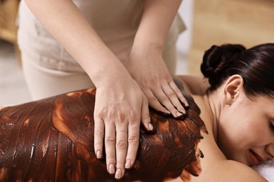 Photo of Woman undergoing chocolate body wrap treatment in spa salon, closeup