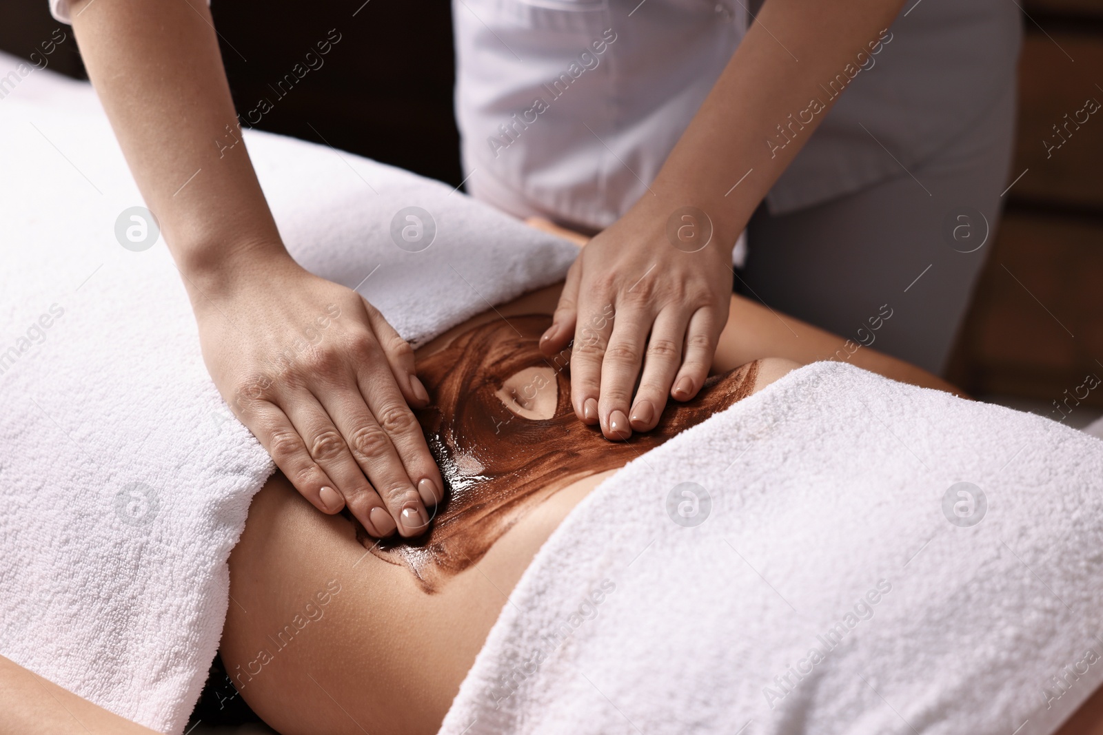 Photo of Woman undergoing chocolate body wrap treatment in spa salon, closeup