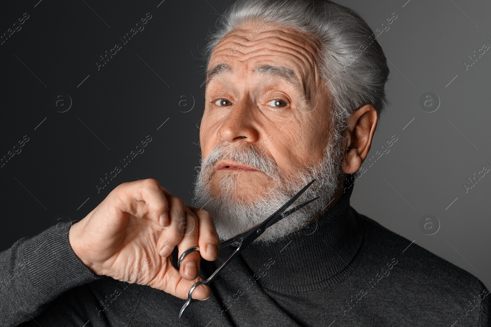 Photo of Senior man trimming beard with scissors on grey background