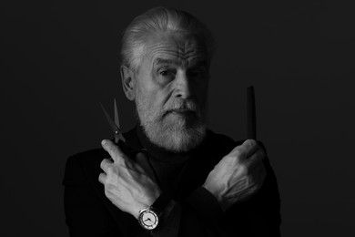 Photo of Bearded man with scissors and comb on dark background. Black and white effect