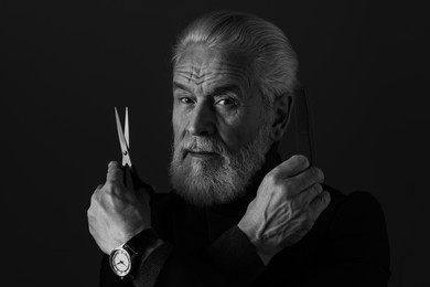 Photo of Bearded man with scissors and comb on dark background. Black and white effect