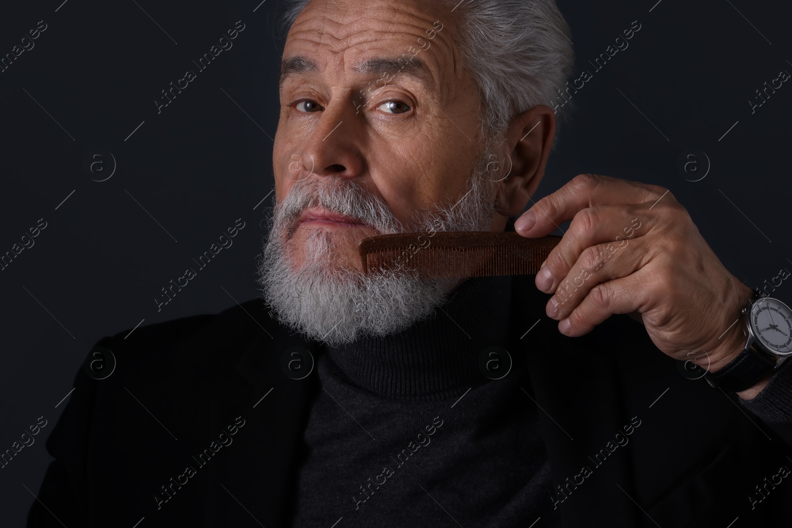 Photo of Senior man combing beard on dark grey background