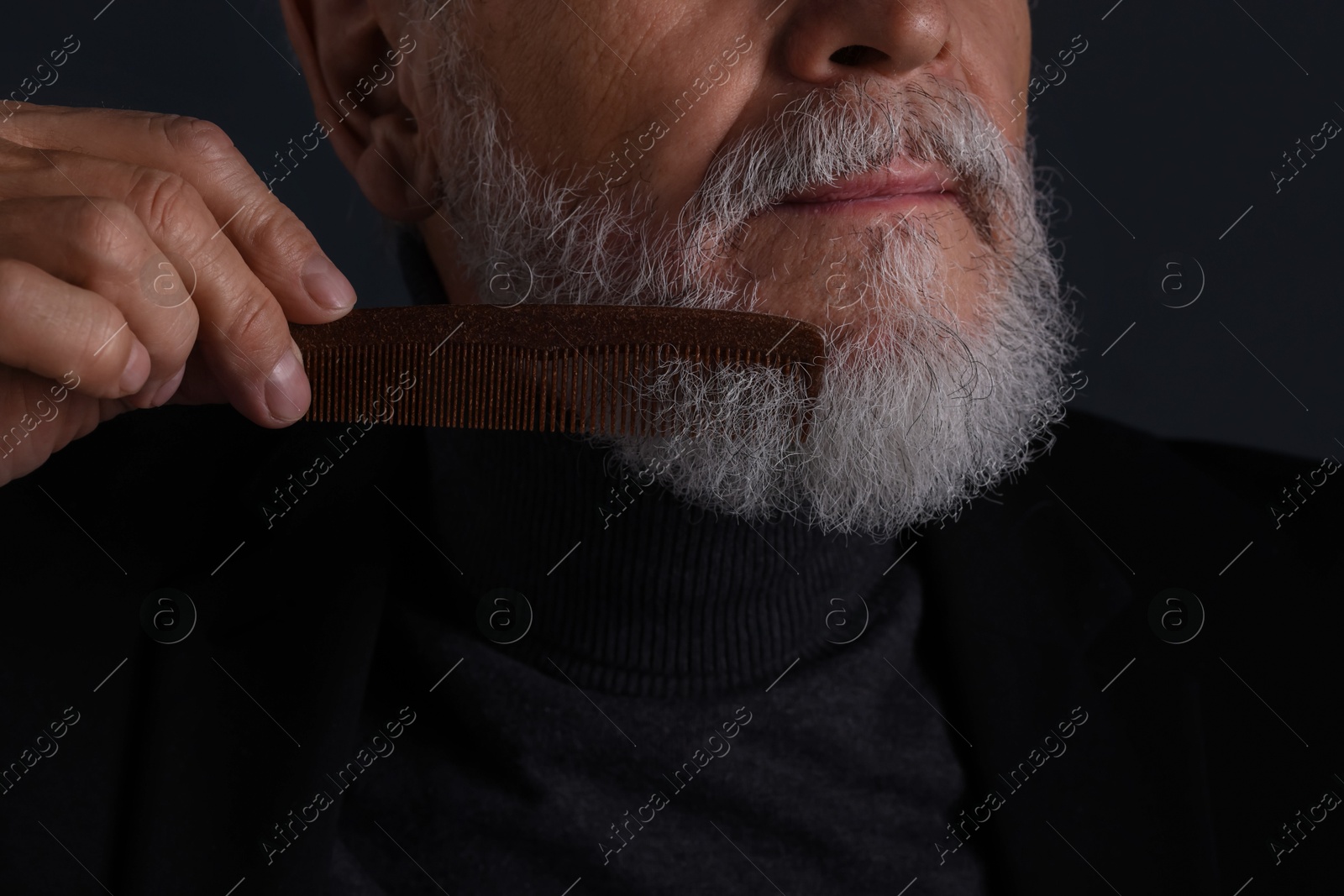 Photo of Senior man combing beard on dark grey background, closeup