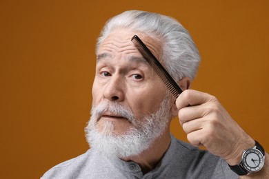 Photo of Bearded senior man combing eyebrow on orange background