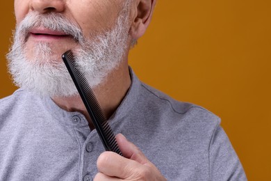 Photo of Senior man combing beard on orange background, closeup