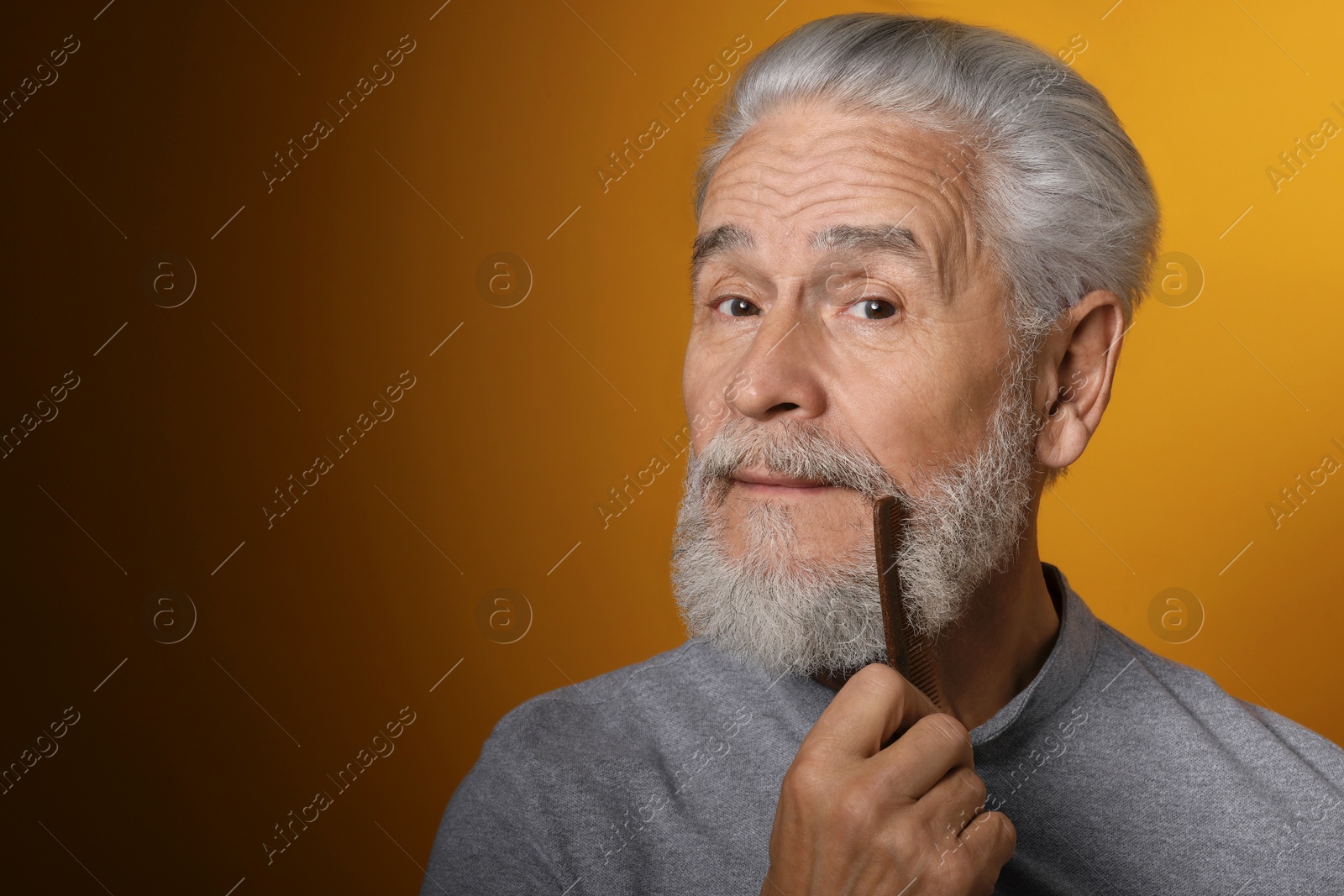 Photo of Senior man combing beard on orange background, space for text