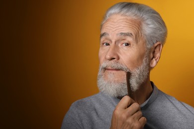 Photo of Senior man combing beard on orange background, space for text