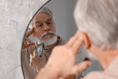 Senior man trimming beard near mirror in bathroom