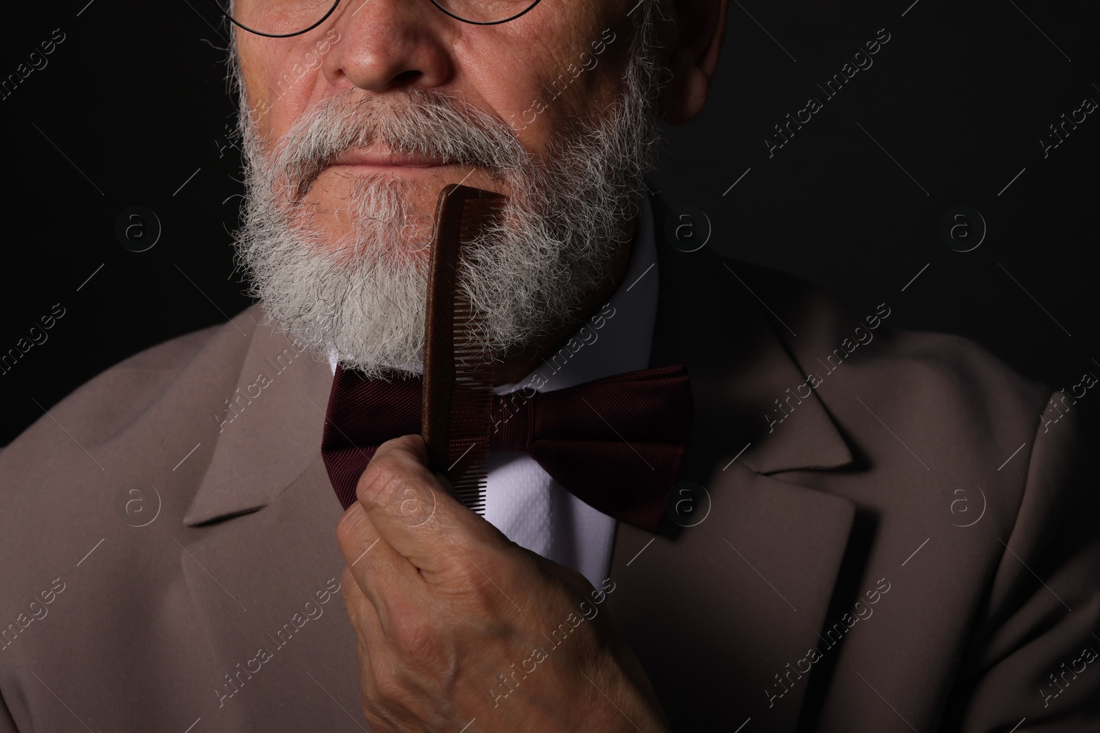 Photo of Senior man combing beard on black background, closeup