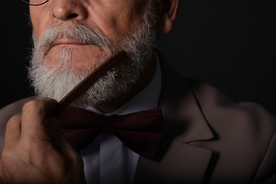 Photo of Senior man combing beard on black background, closeup