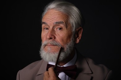 Senior man combing beard on black background