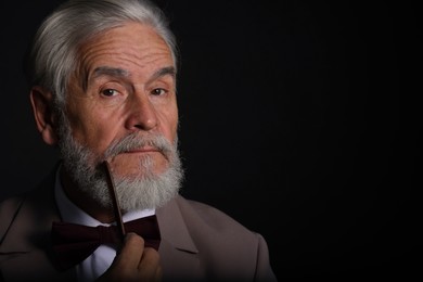 Senior man combing beard on black background, space for text