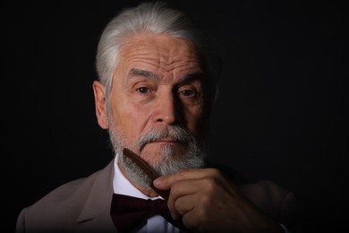 Photo of Senior man combing beard on black background