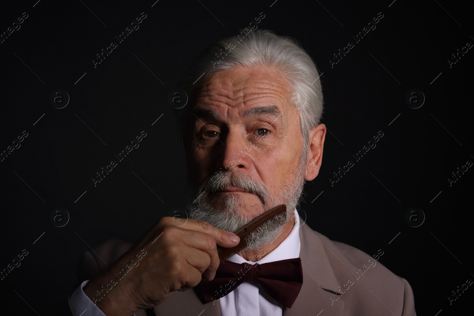 Photo of Senior man combing beard on black background