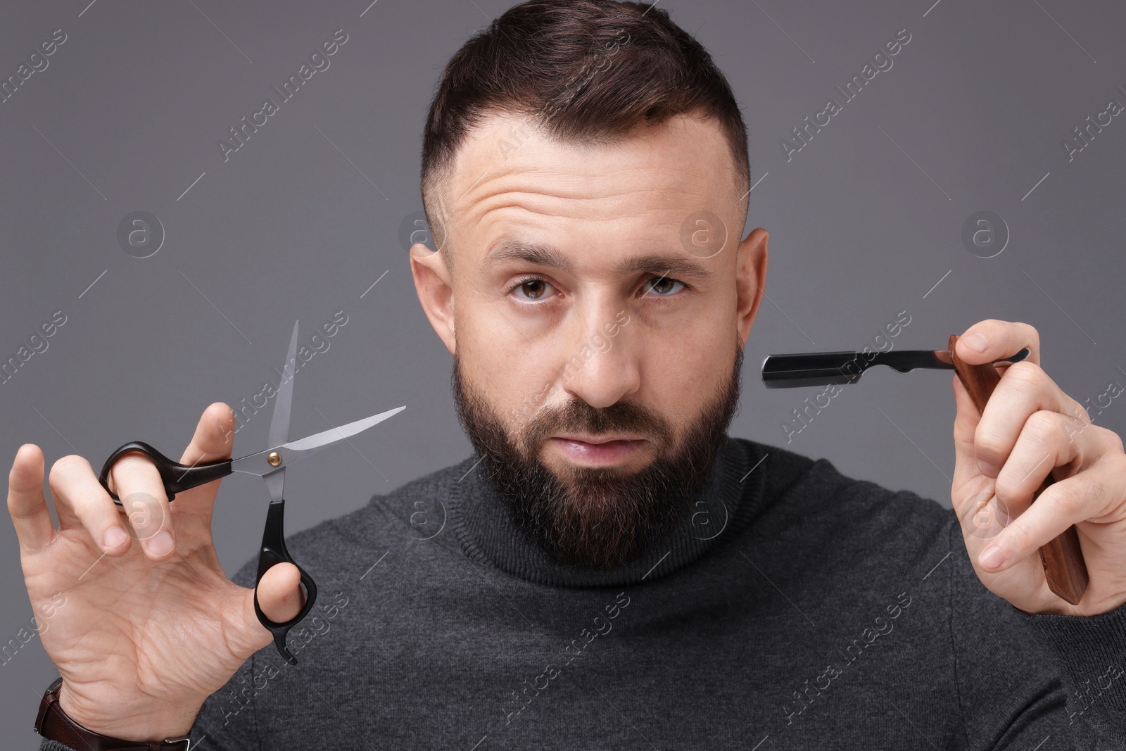 Photo of Bearded man holding blade and scissors on grey background